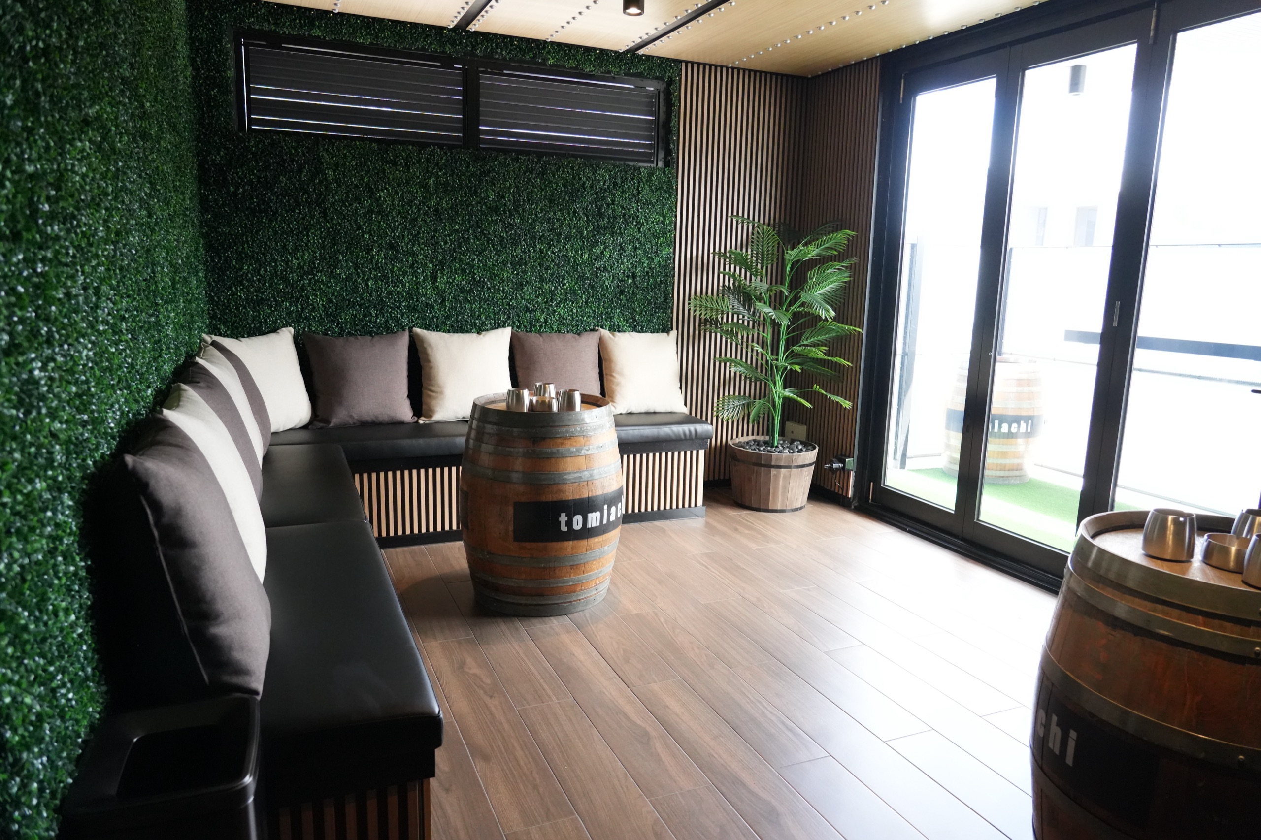 Tomiachi’s garden room with green walls, built-in seating and barrel tables